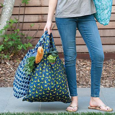 woman in jeans carrying 2 blu bags which are reusable shopping bags with stylish prints and designs